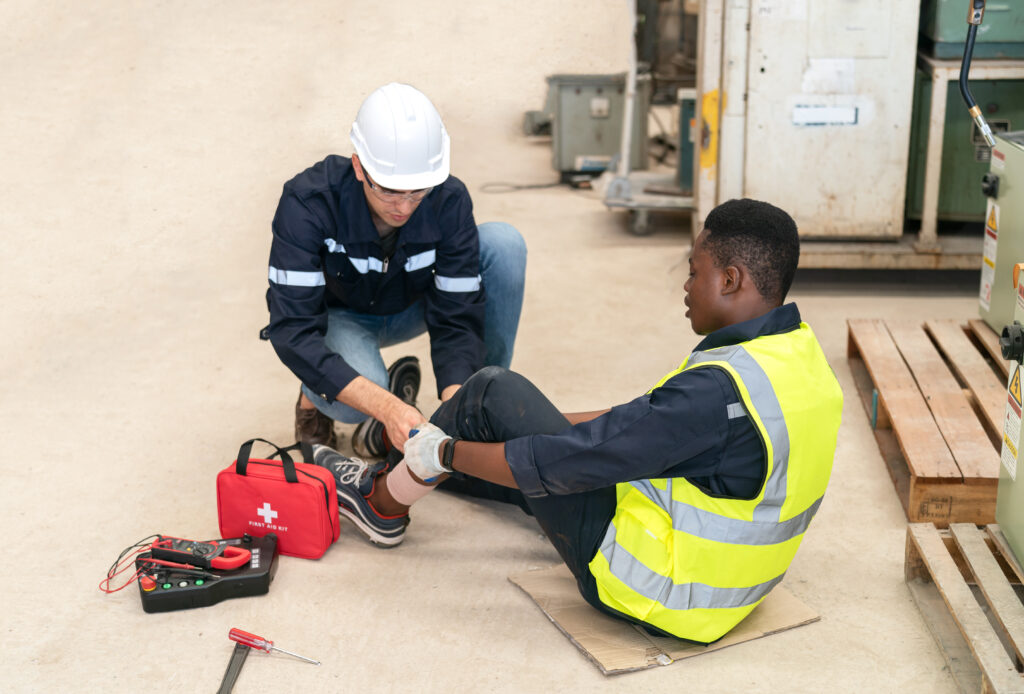 A man helps another man bandage up his leg after a workplace injury before an incident report